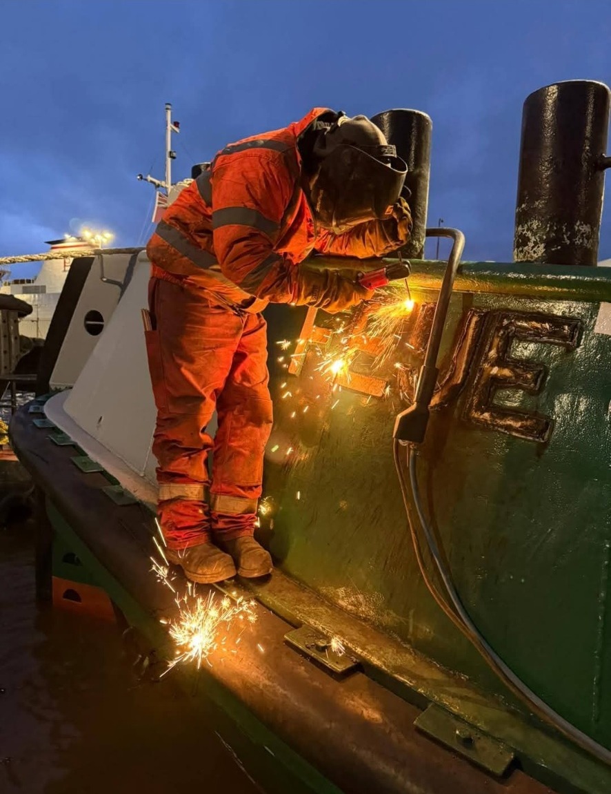Coded welder working on a vessel hull at dusk